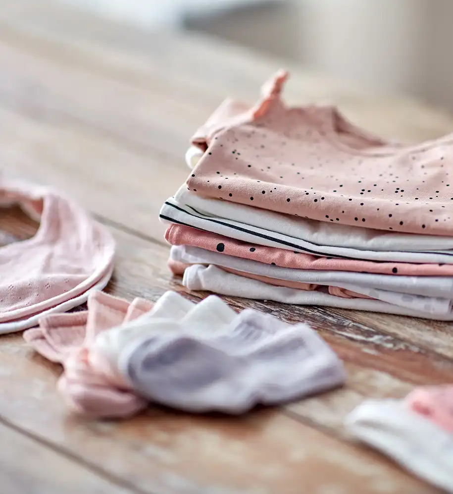 Verschiedene Kinderbekleidungsstücke in Pastelltönen auf einem Holztisch