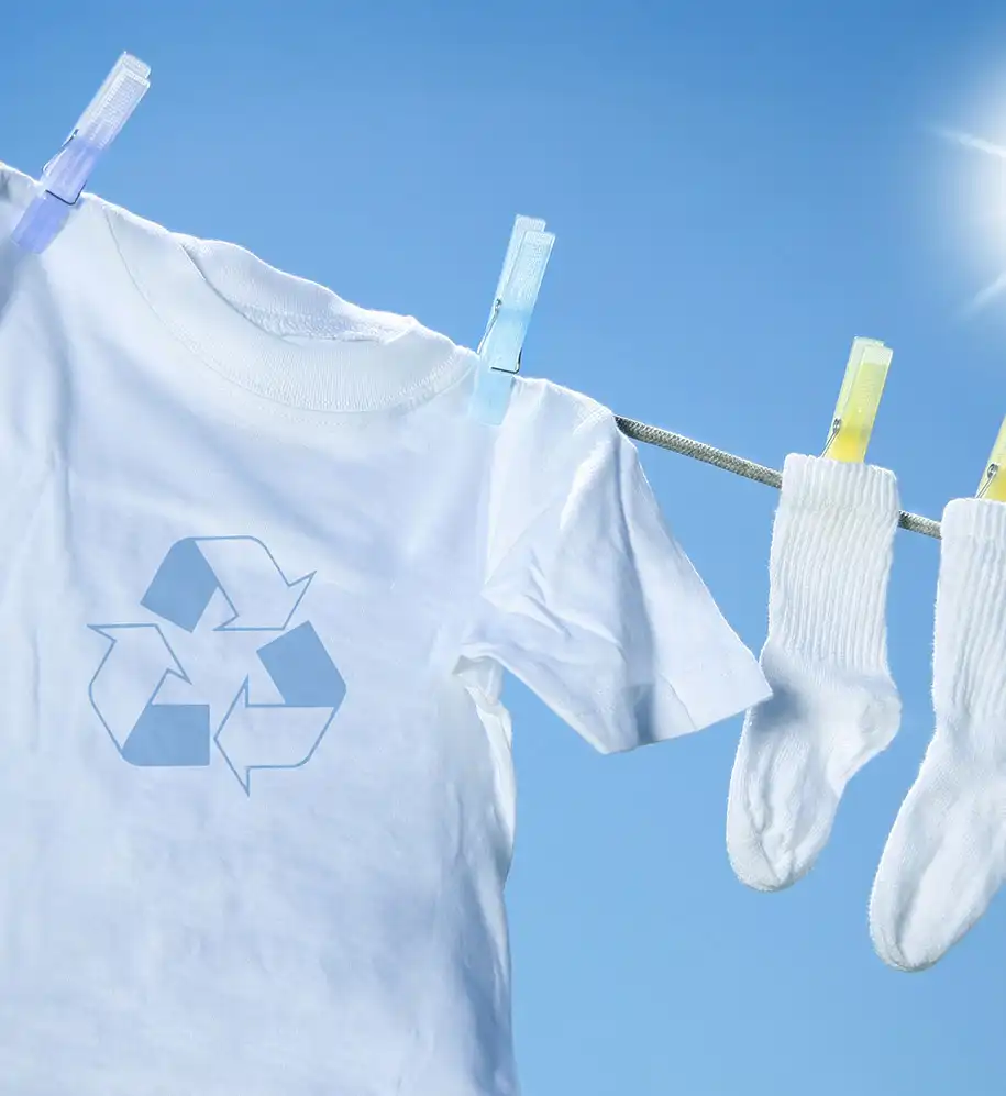 Weißes T-Shirt mit Recyclingsymbol und weiße Socken auf einer Wäscheleine vor blauem Himmel