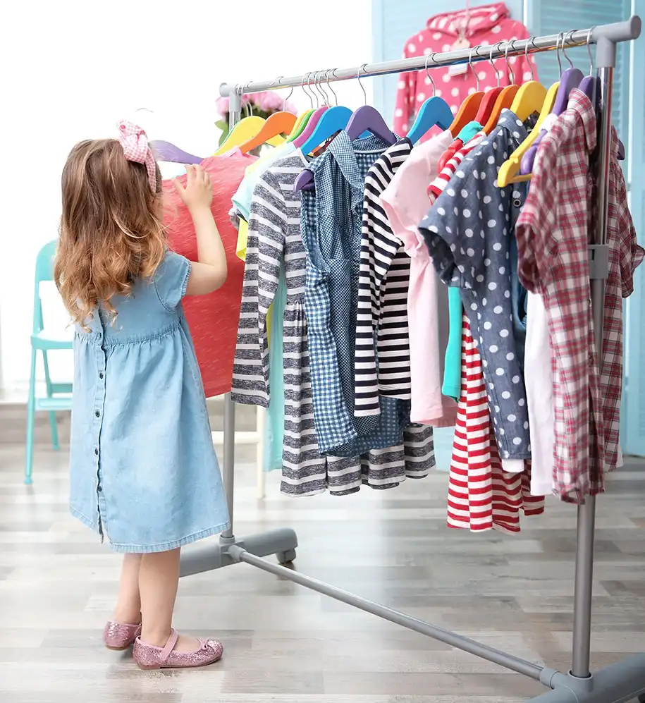 Kleines Mädchen vor Kinderkleidung auf einem Kleiderständer