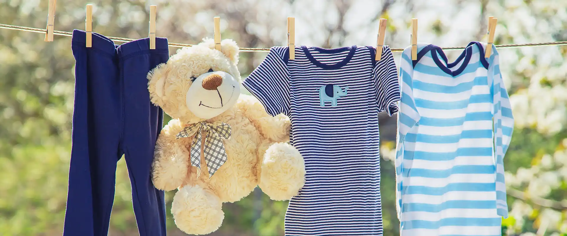 Kinderbekleidung hängt mit einem fröhlich schauenden Teddybär auf der Wäscheleine